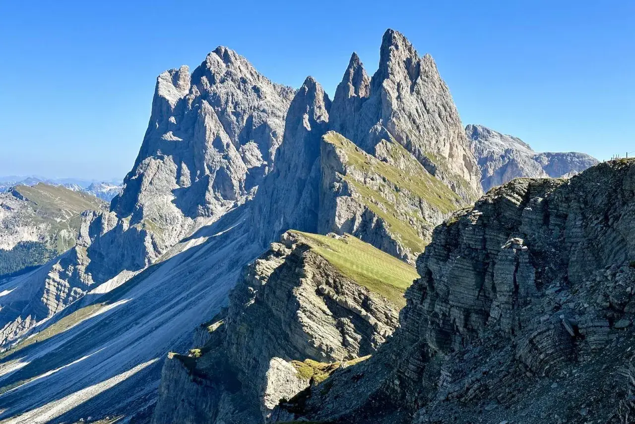 Majestätische Felszinnen ragen in den blauen Himmel. Eine **Seceda Wanderung** führt durch grüne Almwiesen und felsiges Gelände.