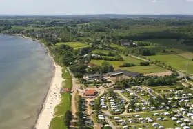 Luftaufnahme eines Campingplatzes in Schleswig-Holstein mit Wohnmobilen und Zelten, direkt am sandigen Strand und dem Meer gelegen.
