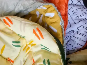 Bunte Muster auf einem Schlafsack aus Baumwolle oder Polyester. Ein gelber Stoff mit orangen und grünen Streifen, daneben ein orangefarbener und ein weißer Stoff mit schwarzen Punkten.