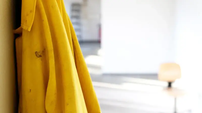 Gelbe Regenjacke hängt an einer Wand, bereit für die Regenjacke reparieren. Flecken auf dem Stoff deuten auf vergangene Abenteuer hin.