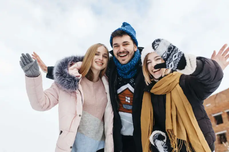 Drei Freunde genießen das Wandern im Winter. Sie tragen warme Kleidung wie Daunenjacken, Mützen und Handschuhe.